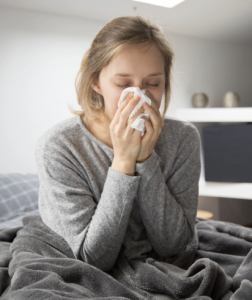 sick woman sitting in bed, blowing nose with napkin